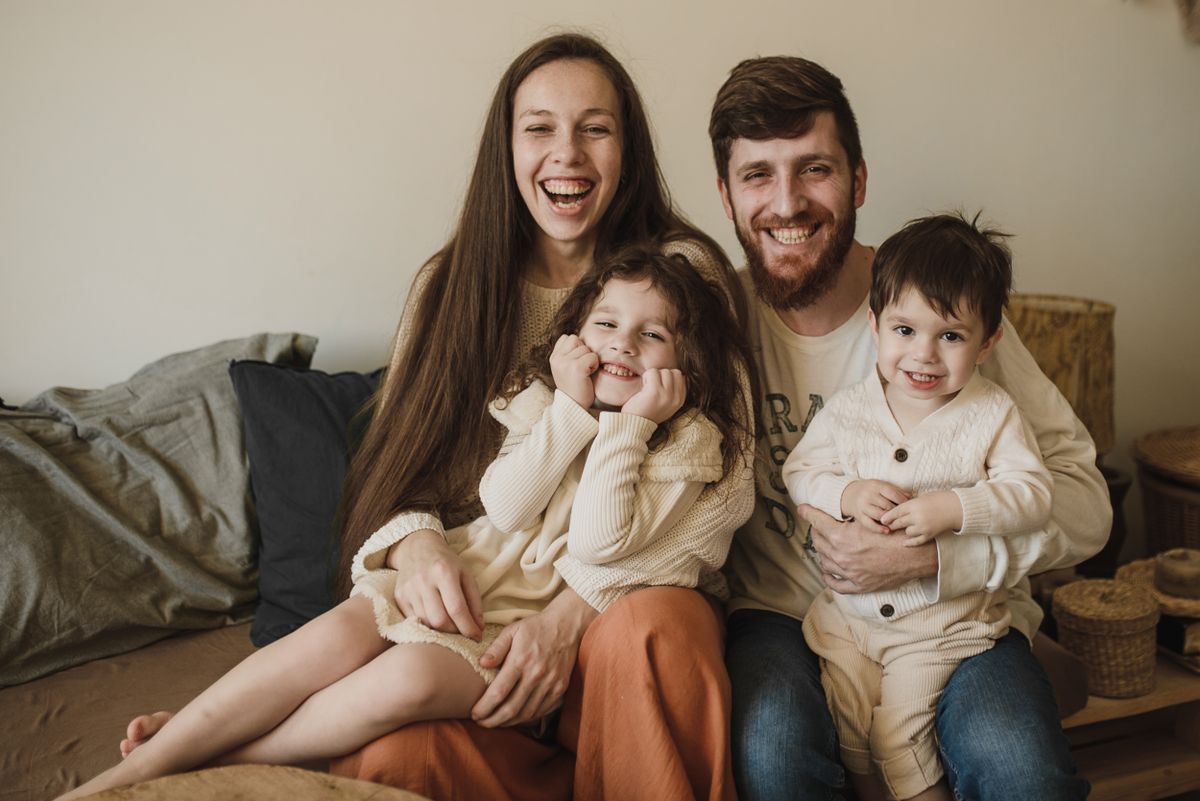 Pais sorrindo com seus dois filhos no sofá de casa